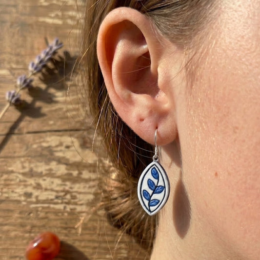 Close-up of an ear wearing a floral earring with a wooden surface and lavender in the background