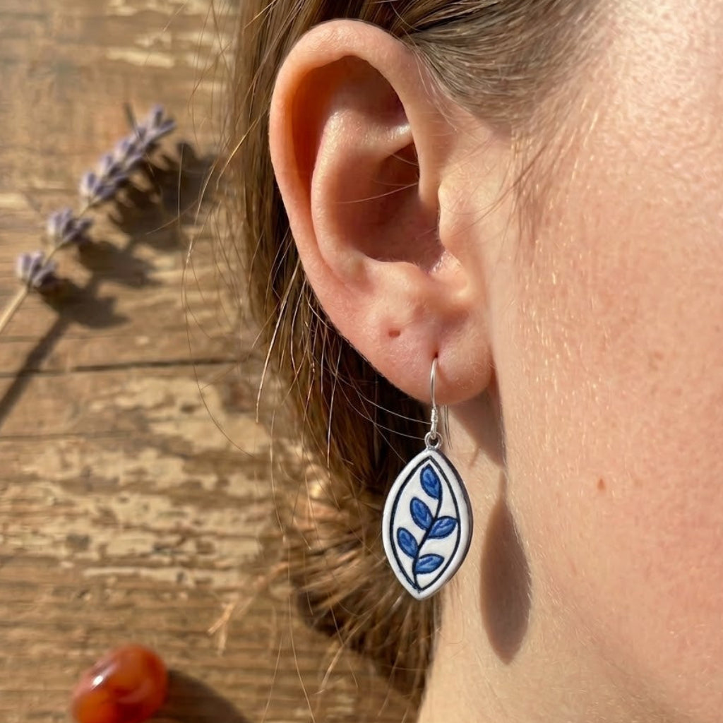 Close-up of an ear wearing a floral earring with a wooden surface and lavender in the background
